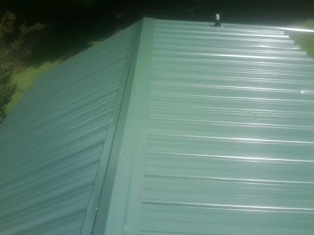 New green metal panels meeting at the ridge of a roof — Flat Roof Repair work by our crew in Temple