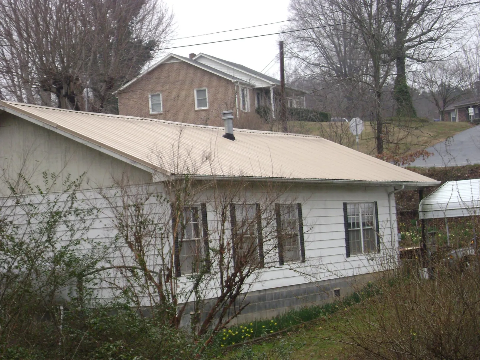 Tan metal roof on a white sided house set into a hillside — Commercial Roofing by Roofing Brothers in Temple